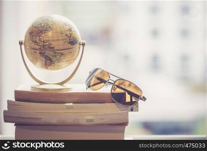 Miniature globe model and sunglasses lying on a stack of books. Symbol for travelling.