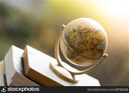 Miniature globe model standing on a stack of books. Symbol for travelling.