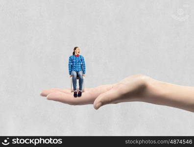 Miniature of teenager girl. Young woman sitting in chair on female palm