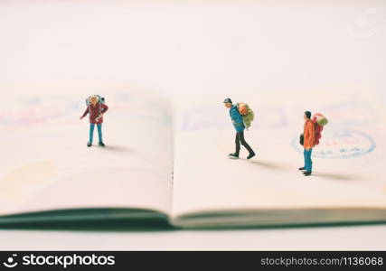 Miniature people figures with backpack walking and standing on passport page with immigration stamps, travel and vacation concept