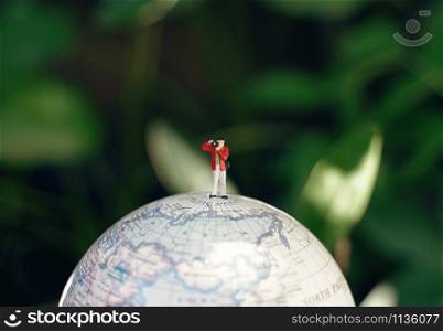 Miniature people photographer figures with camera standing on globe model, travel and photography concept