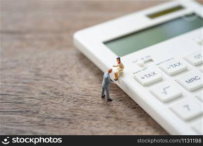 Miniature people sitting on white calculator using as background business concept and teamwork concept with copy space and white space.