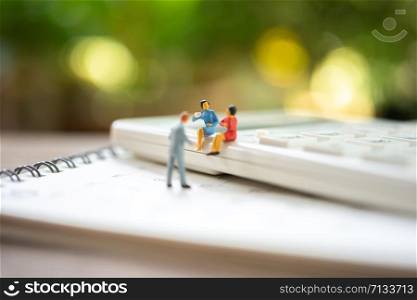 Miniature people sitting on white calculator using as background business concept and teamwork concept with copy space and white space.