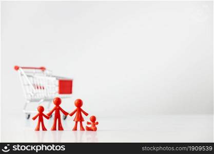 Miniature plastic figures family with children and Metallic shopping cart trolley on light gray background with copy space. Miniature plastic figures family with children and Metallic shopping cart trolley on light gray background