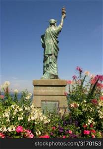Miniature Statue Of Liberty Replica Surrounded By Tropical Flowers And Looking Out To Sea