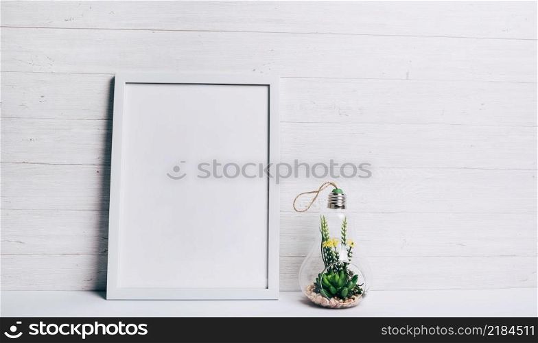 miniature succulent plant inside glass hang lamp near white frame against wooden wall
