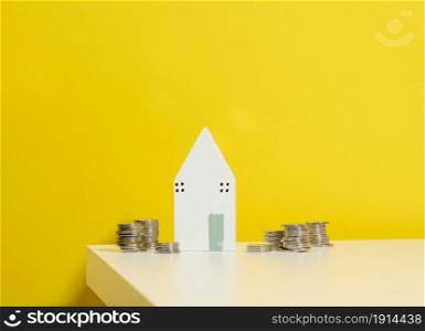 miniature wooden house and a stack of coins on a white table. Real estate purchase, mortgage concept. Rise in real estate prices, subsidies from the state