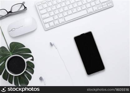 Minimal Office desk table top view with Smart phone, Earphones, Keyboard computer, mouse, Glasses,  coffee cup on a white table with copy space, White color workplace composition, flat lay