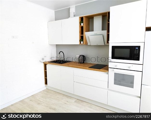 Minimal white kitchen modern scandinavian interior with cooker hood on wooden countertop. Real photo. White kitchen scandinavian interior with cooker hood on wooden countertop