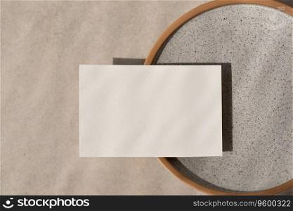 Minimalist business brand template, blank paper card mockup on ceramic plate, on a beige stone background in sun light, wedding invitation or greeting card design. Minimalist business brand template, blank paper card mockup on ceramic plate, on beige stone background in sun light, wedding invitation or greeting card design
