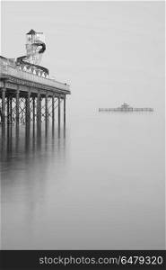 Minimalist fine art landscape image of new pier in juxtaposition. Minimalist fine art image of new pier in juxtaposition with old derelict pier in background in black and white