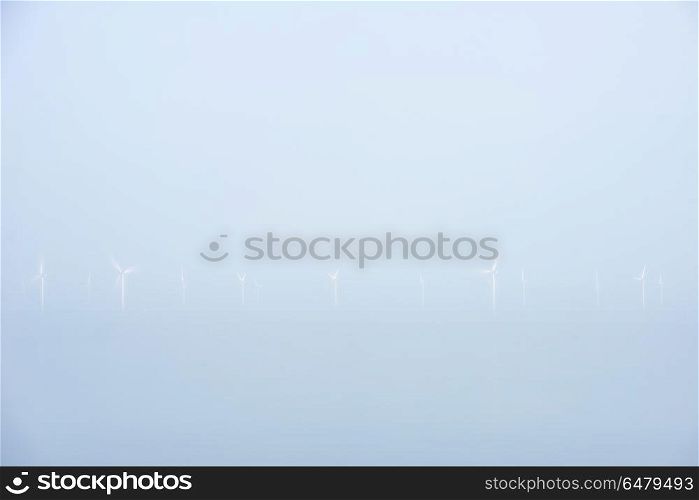 Minimalist landscape image of wind turbines at sea in low lying . Very minimalist landscape image of wind turbines at sea in low lying mist cloud