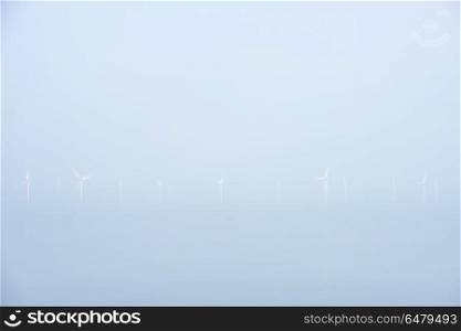 Minimalist landscape image of wind turbines at sea in low lying . Very minimalist landscape image of wind turbines at sea in low lying mist cloud