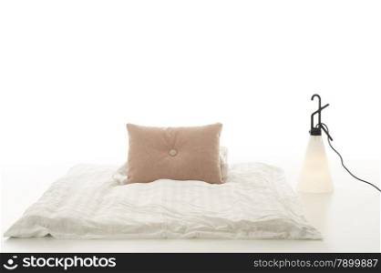 Minimalist modern living area. Minimalist modern living area with a comfortable soft plain white comforter with beige cushion on the floor alongside a contemporary design conical lamp over a white background with copyspace