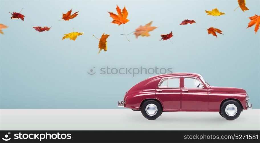 Minimalistic autumn car. Autumn red toy car with fallen leaves against minimalistic blue background