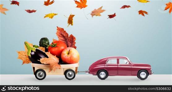 Minimalistic food delivery. Food delivery. Autumn red toy car with fallen leaves delivering fruits and vegetables against minimalistic blue background