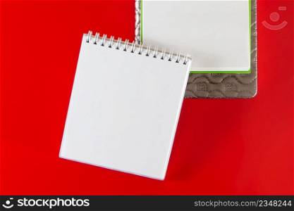 Minimalistic layout for design. Office supplies - notebooks and pens on a red background. Open blank notebook for your notes on a red background. Minimalistic layout for design. Office supplies - notebooks and pens on a red background.