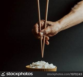 Minimalistic old hands grabbing japanese chopsticks over a bowl of rice concept shot on cinematic tones over a black background