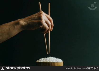 Minimalistic old hands grabbing japanese chopsticks over a bowl of rice concept shot on cinematic tones over a black background