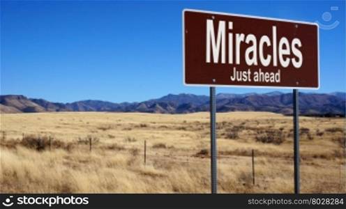 Miracles Just Ahead brown road sign with blue sky and wilderness