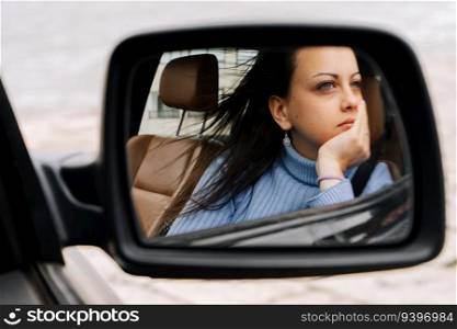 Mirror portrait of a young woman sitting on the passenger seat of a car
