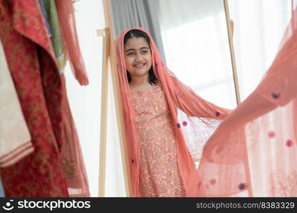 Mirror reflection of Indian little cute kid girl in traditional clothing smiling at mirror with beautiful clothes she choosed while dressing at home