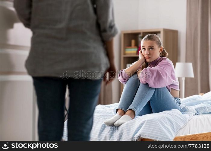 misbehavior, conflict and family concept - mother entering room and sad daughter sitting on bed at home. mother and sad daughter sitting on bed at home