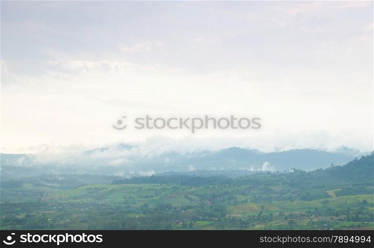 Mist covered mountains and farmland. In the evening, a cold and is nearly dark.