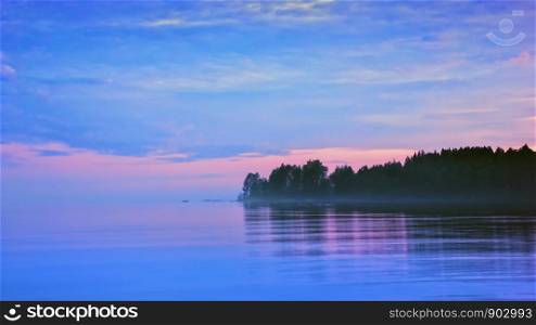 Misty lilac seascape with pink and blue clouds reflecting in a flowing water. Midnight on the forested shore of Lake Onega in the White Nights season, Karelia, Russia. Blurred natural background with copy space, soft selective focus.