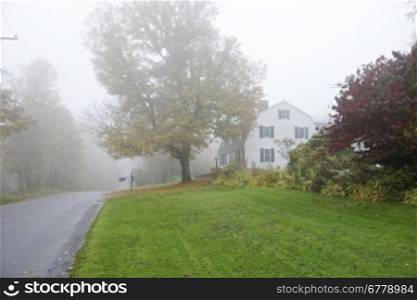 Misty morning, Autumn / Fall Foliage. Country side view with wooden house with a car on the road