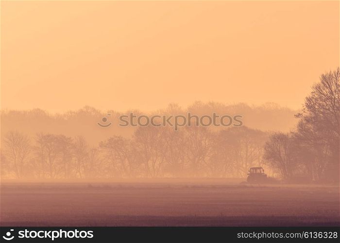 Misty morning with a tractor on a field in the sunrise