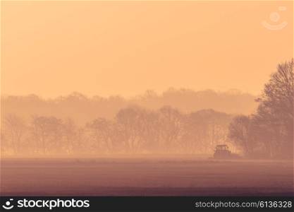 Misty morning with a tractor on a field in the sunrise