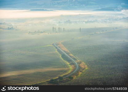 Misty road through fields against sunset