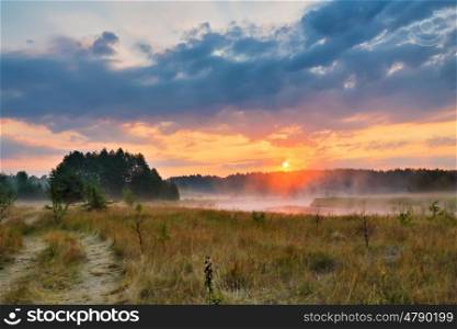 Misty summer sunrise. Foggy river in the morning. Colorful summer morning. Dirt road at summer morning riverbank