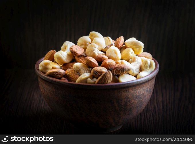 Mix of cashews and almonds in a clay plate on a dark wooden background. Mix of cashews and almonds in clay plate