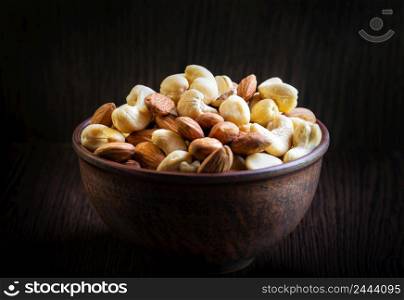 Mix of cashews and almonds in a clay plate on a dark wooden background. Mix of cashews and almonds in clay plate