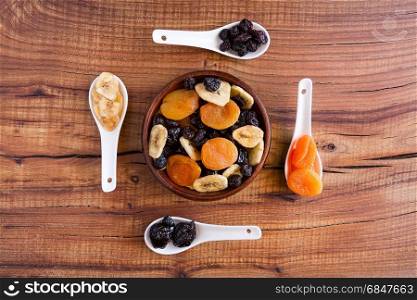 Mix of dried fruits in a wooden bowl over a rustic table seen from above. Mix of dried fruits in a wooden bowl over a rustic table