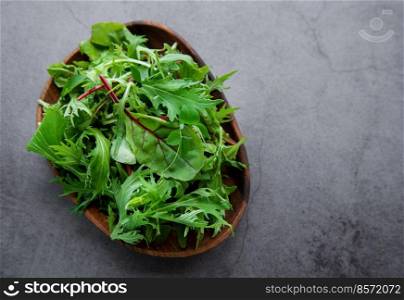 Mix of fresh green salad leaves with arugula and beets in plate on dark concrete background. Ingredient for healthy  salads  