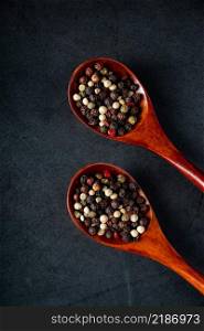Mix of red and black pepper in wooden spoon on a black background. Aromatic spice for cooking.. Mix of red and black pepper in wooden spoon on black background. Aromatic spice for cooking.