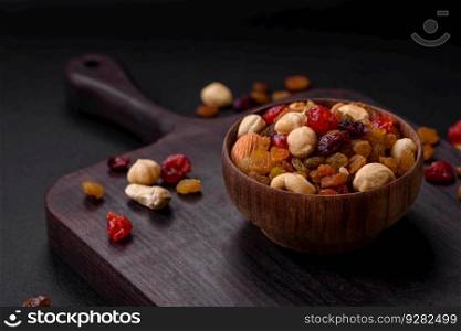 Mix of roasted cashews, hazelnuts and walnuts with dried cranberries and raisins on a dark concrete background