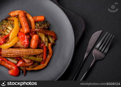 Mix of vegetables corn, carrots, peppers, broccoli, onions in teriyaki sauce on a ceramic plate on a dark concrete background