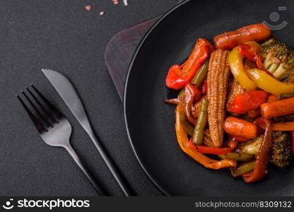 Mix of vegetables corn, carrots, peppers, broccoli, onions in teriyaki sauce on a ceramic plate on a dark concrete background