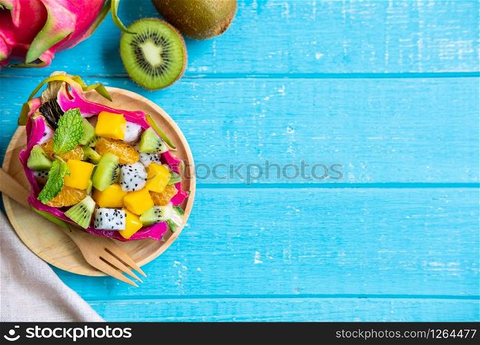 Mix tropical fruits salad served in half a dragon fruit on wooden table with copy space. Mix tropical fruits salad served in half a dragon fruit on wooden table