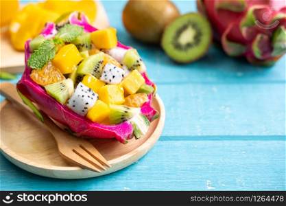 Mix tropical fruits salad served in half a dragon fruit on wooden table