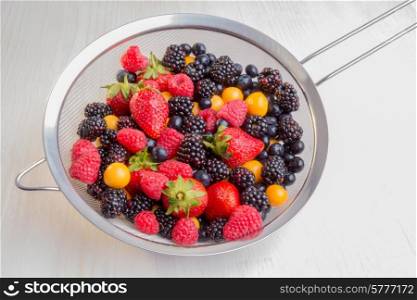 Mixed berries of different types, colors, and shapes in a colander.