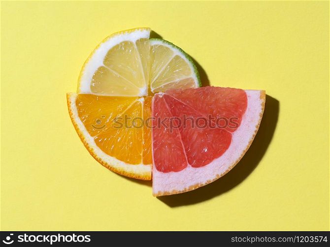 Mixed citrus fruits slices in sunlight, on yellow background. Fresh citrus fruits cut in quarters, displayed in a circle. Summer fresh fruits.