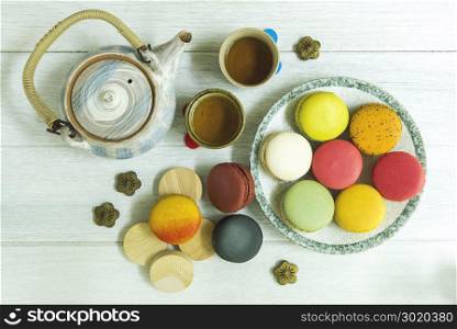 Mixed colorful french macaroons on plate and wooden table with teapot.