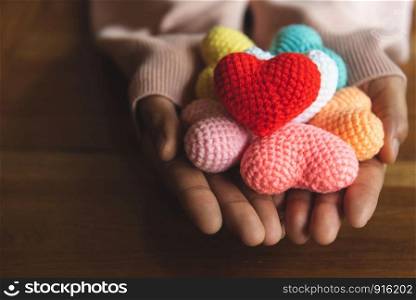 Mixed colors yarn heart on giving hands. Close up of colorful handmade. Heart donation concept. Valentine love forever theme