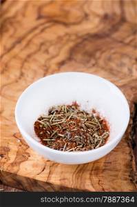 Mixed dried herbs with paprika in small bowl over olive wood background, selective focus