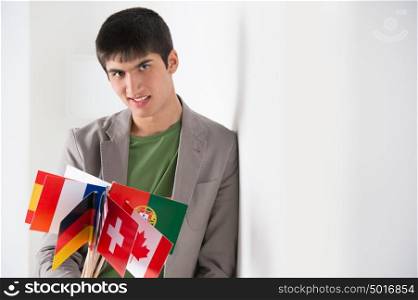 Mixed ethnicity handsome man leaning on white wall and holding many countries flags